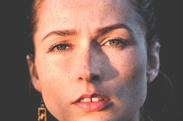 Image of a woman's face that is half illuminated by the sun.  she has freckles and green eyes